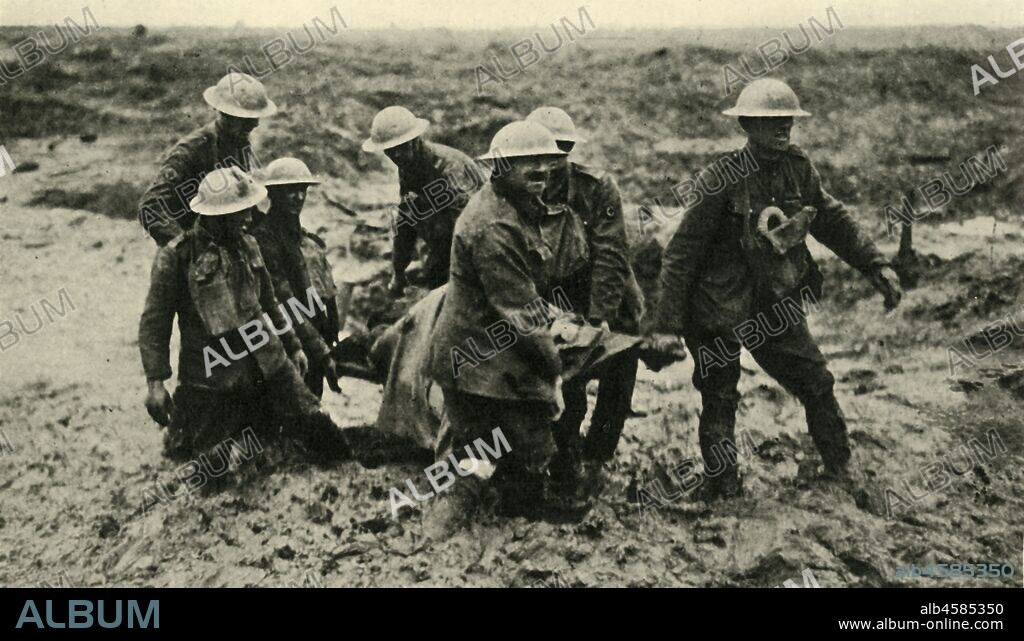 'Red Cross Work in the Flanders Mud', First World War, 1 August 1917, (c1920). 'R.A.M.C. stretcher-bearers bringing in wounded during the advance on Passchendaele'. Royal Army Medical Corps personnel struggle in mud up to their knees to carry a wounded man to safety near Boezinge during the Battle of Pilckem Ridge. The appalling conditions on the Belgian Western Front were caused by heavy rain which created seas of thick mud. From "The Great World War: A History", Volume VII, edited by Frank A Mumby. [The Gresham Publishing Company Ltd, London, c1920].