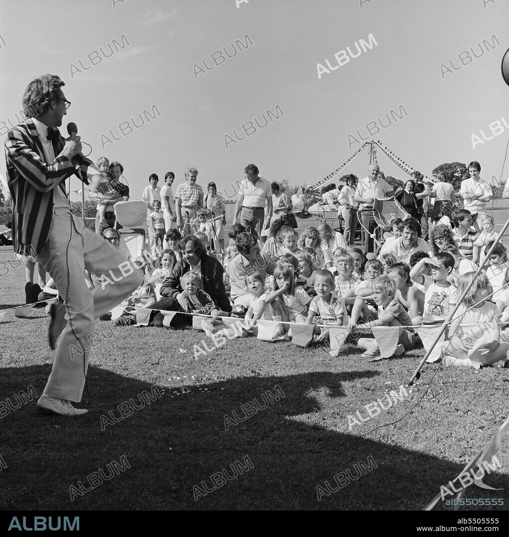 JOHN LAING PLC. Laing Sports Ground, Rowley Lane, Elstree, Barnet, London, 21/06/1986. A man in a striped jacket, possibly 'Poz the Magician,' entertaining a crowd of children at the 1986 Family Day at Laing's Sports Ground. Over 2500 people attended the Family Day and raised over £700 for that year's designated charity The British Heart Foundation.  Attractions included; guest appearances by the cast of the television programme Grange Hill, a bouncy castle, donkey rides, Punch and Judy shows, Pierre the Clown, children's races, blindfold stunt driving and golf and six-a-side football tournaments.