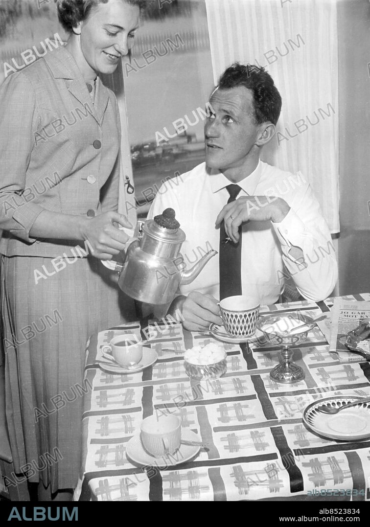 MALMÖ 1960-02.. Orig. bildtext... KAFFETÅREN DEN BÄSTA ÄR, även för en skidkung. Sixten Jernberg blir serverad av fru Kerstin. Anm. S. Jernberg, 1929, skidåkare, den svensk som har flest OS-medaljer, 9 st Kaffebord Kaffekoppar Sockerskålar Vaxdukar Kaffepannor Virkade lockskydd Dräkter Plisserad kjol Rutig Form Design CD356 persons: KERSTIN JERNBERG;SIXTEN JERNBERG sites: SVERIGE;MALMÖ.