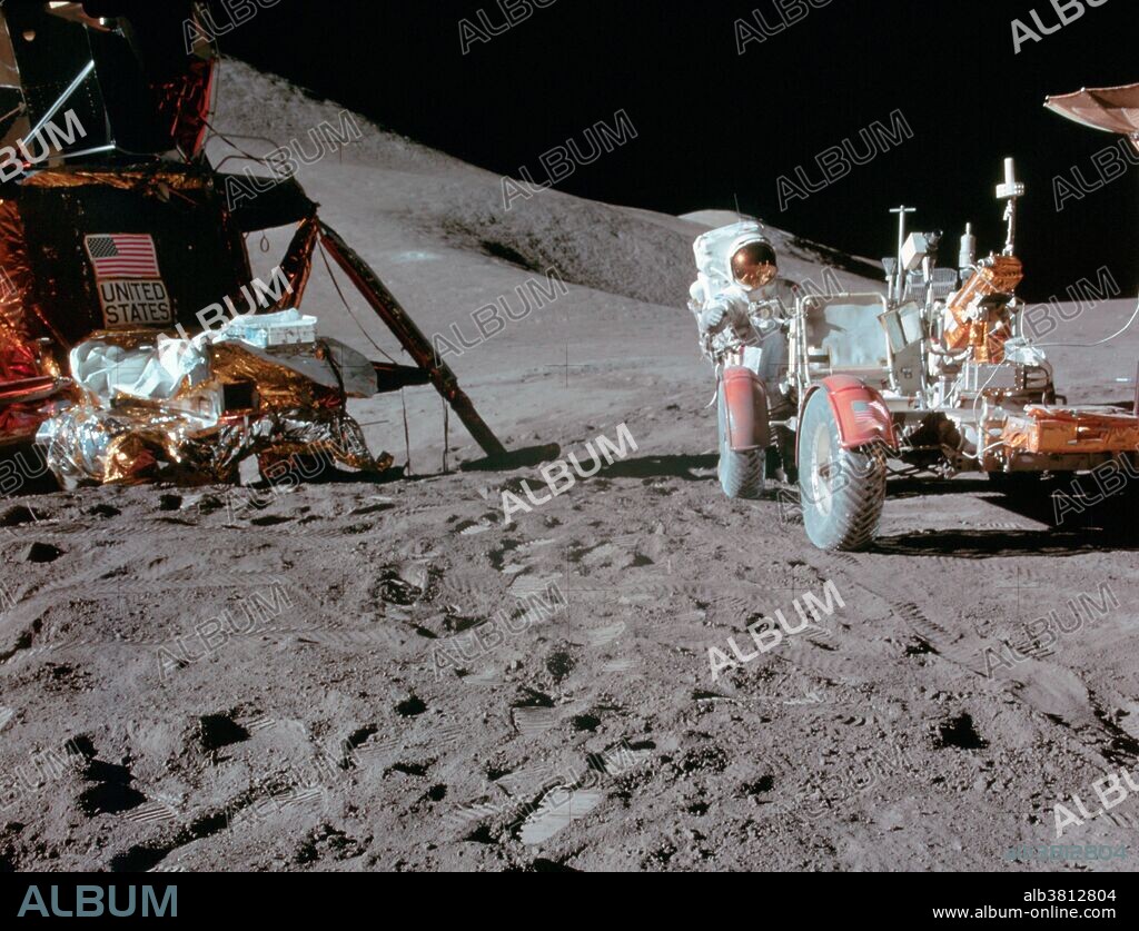 Astronaut James B. Irwin, lunar module pilot, works at the Lunar Roving Vehicle (LRV) during the first Apollo 15 lunar surface extravehicular activity (EVA) at the Hadley-Apennine landing site on July 31, 1971. The Lunar Module (LM) "Falcon" is on the left. The undeployed Laser Ranging Retro Reflector (LR-3) lies atop the LM's modular equipment stowage assembly (MESA). This view is looking slightly west of south. Hadley Delta and the Apennine Front are in the background to the left. St. George crater is approximately five kilometers (about three statute miles) in the distance behind Irwin's head. This photograph was taken by astronaut David R. Scott, commander. While astronauts Scott and Irwin descended in the LM to explore the moon, astronaut Alfred M. Worden, command module pilot, remained with the Command and Service Module (CSM) in lunar orbit.