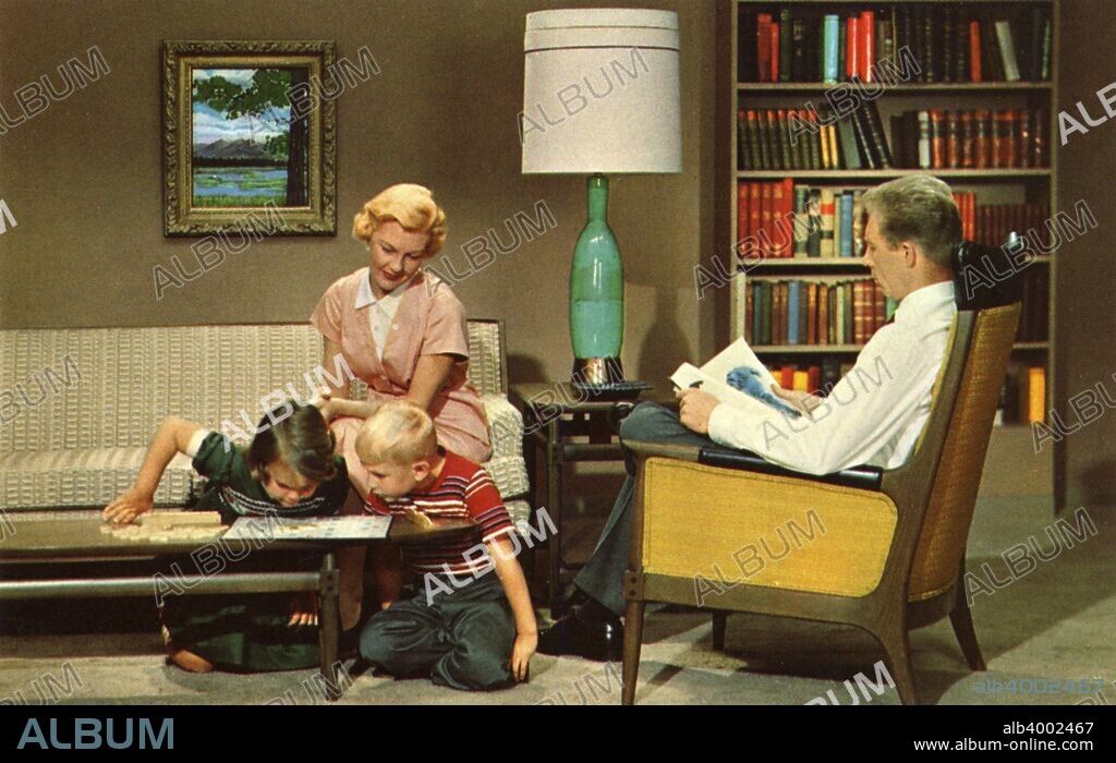 Family sitting in their living room, USA, 1962. The children play a game of Scrabble while mother watches and father reads the newspaper.
