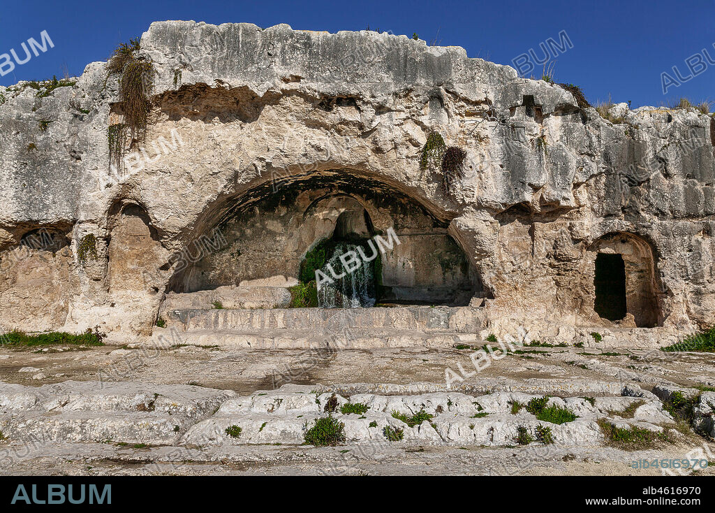 Syracuse, The Archaeological Park of the Neapolis of Syracuse: the Grotta del Ninfeo, built in the second century BC.The grotta is located near the highest part of the little rocky relief, on a rectangular terrace which verges on the Greek theatre and opens at the centre of a stone wall where a closed portico in the form of an "L" was once found. At the entrance there were statues dedicated to the Muses, three of which (dated to the 2nd century BC) are still preserved and are on display at the Museo Archeologico Regionale Paolo Orsi. The fountain is dedicated to the Ancient Greek cult of the nymphs, nature goddesses. The name nymphaeum for a monumental, decorated fountain derives from this. The Syracusan nymphaeum is thought to have been the ancient location of the Mouseion (the sanctuary of the Muses), seat of the artistic guild, where the Syracusan actors gathered before descending into the theatre to put on comedies and tragedies in the time of Epicharmus and Aeschylus.
