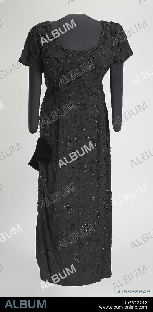 Ella Jane Fitzgerald (1917-1996) was an African-American jazz singer, sometimes referred to as the First Lady of Song, Queen of Jazz, and Lady Ella. The dress is made from black synthetic crepe fabric that is hand beaded with black glass seed and bugle beads, and black sequins in a floral vine design. The bodice is short-sleeved and has a scoop neck in the front and a V-neck in the back. There is a metal zipper in the center back that goes to the hip, and a hook-and-eye at the top of the zipper. The gown has a princess cut waist, but there is no seam at the waist. The gown has a column skirt with a slit on the proper right side that is 24 1/2" high and contains a rounded hem. At the top of the slit, there is a pre-tied black velvet bow that is sewn to the dress.