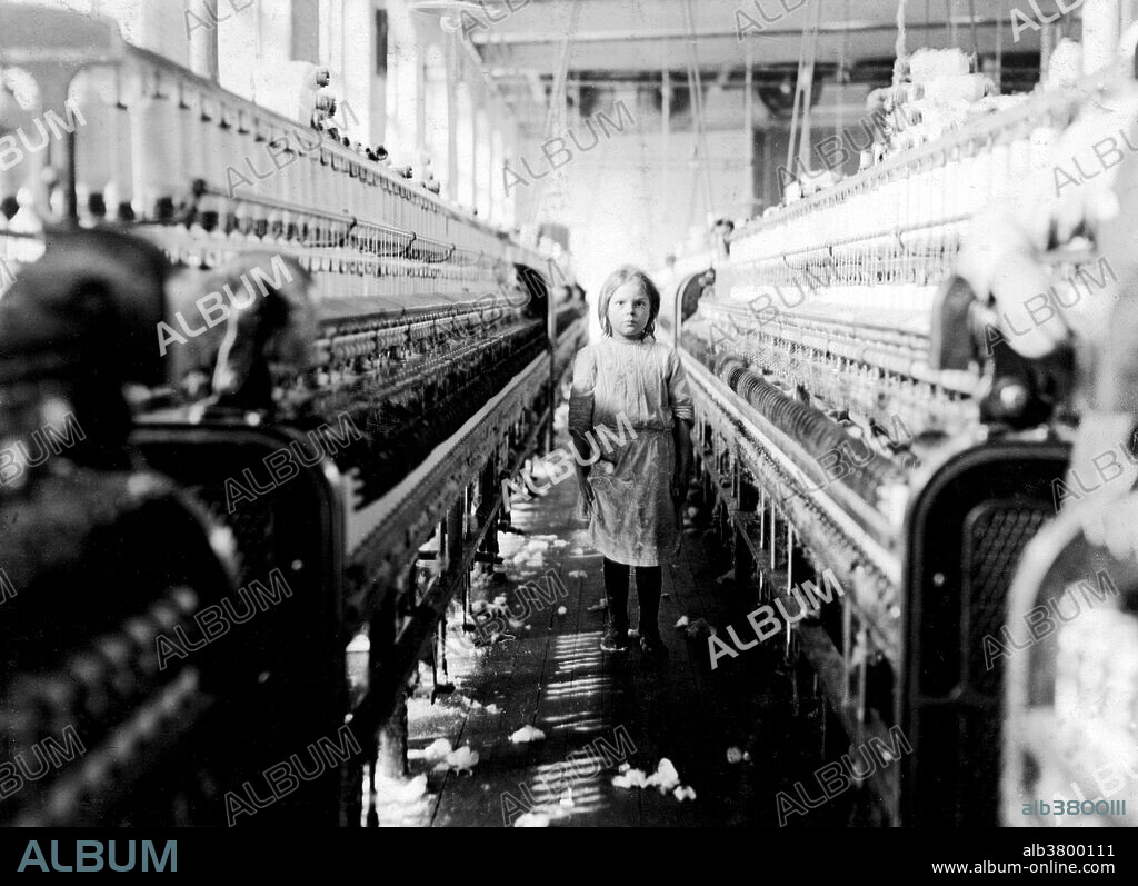 Entitled: "A little spinner in the Mollahan Mills. She was tending her sides like a veteran, but after I took the photo, the overseer came up and said in an apologetic tone that was pathetic, "She just happened in." Then a moment later he repeated the information. The mills appear to be full of youngsters that "just happened in," or "are helping sister. Location: Newberry, South Carolina." Cotton mills were designed to move cotton through a precise series of production processes that separated, straightened, and twisted cotton fibers, combined them into yarn, then wove the yarn into cloth. Workers directed four or more slivers through a series of rollers in the head of a drawing frame, where they were combined in a single strand. As bobbins on the spinning frames filled with thread, doffers replaced them with empty ones. The spinner's job was to move quickly up and down a row of machines, repairing breaks and snags. Photographed by Lewis Hine, December 3, 1908.