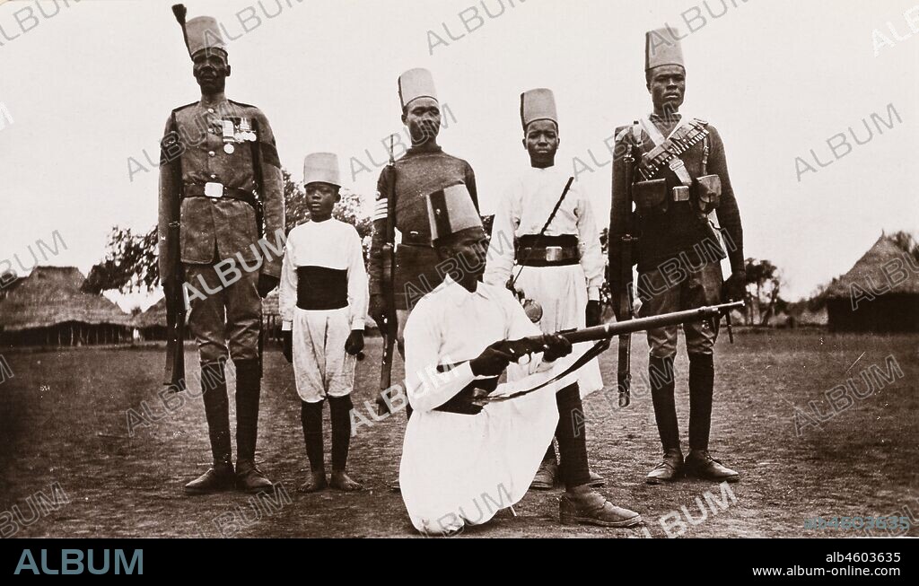 Sudan, Printed caption reads: 'Types of Sudanese Soldiers. Published by G N Morhig, The English Pharmacy, Khartoum. Copyright 81'. Five Sudanese men and a young boy pose for the camera, wearing a variety of Egyptian Army military uniforms. All are dressed in fez hats, their uniform varying according to their station, [c.1906]. 2003/222/1/1/62.