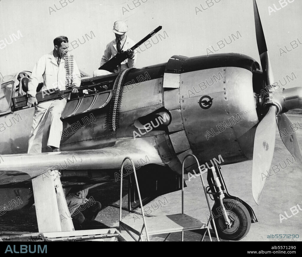 "Heaviest Armed Fighting Ship" -- Mechanics Ted Rich (left) and R.E. Whitney installing two .50-caliber Machine guns in a Vultee Vanguard pursuit plane here recently. These guns fire through the propeller of the plane which engineers of Vultee Aircraft Inc. claim is the "Heaviest armed fighting plane in the world." Tests indicate the 350 M.P.H. plane can handle six .30-Caliber guns on its slim wing, two similar weapons and two .50-caliber guns from its fuselage. With this gun equipment the plane could fire 5,000 rounds without landing. The Barrels and mechanisms of the guns are detachable and fresh guns could be installed in 30 minutes. March 20, 1940. (Photo by Wide World Photo).