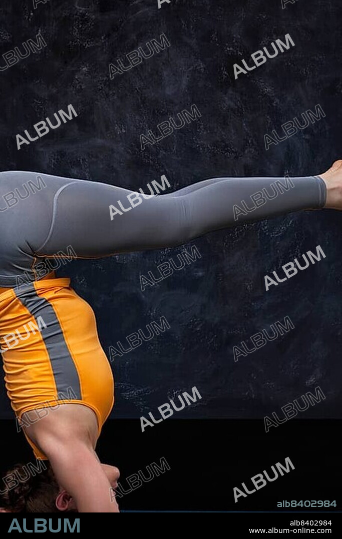 Woman doing Hatha yoga Ashtanga Vinyasa Yoga asana sirsasana, headstand variation Urdhva dandasana, upward facing staff pose on dark grund background.