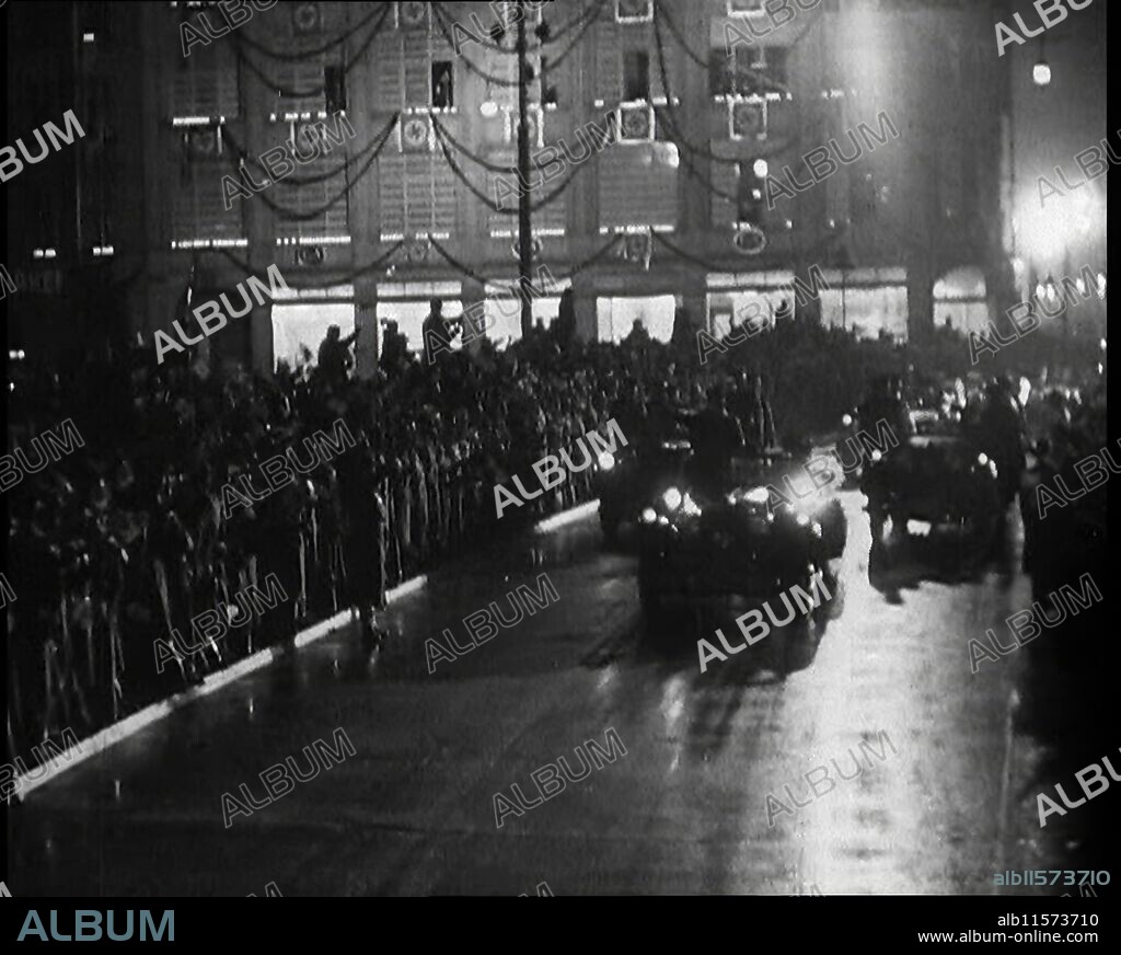 A Nazi Party Motorcade Driving Down a Berlin Street Lined With Crowds And a Large Decorated Building Behind, 1937. 'The leader [Adolf Hitler] returns from his visit to Italy...the people are told that the leader is not just a man, but a flawless god, and must be treated as such - and treated as such he is. Not the return of a conquering hero, for as yet the hero has not set about his real conquests. No, this is just the return of Germany's favourite son. Something new. Something and somebody of a driving force and influence. This, unless it were destroyed, the future power and the glory of a planet. The lord be praised, that in the end it was destroyed, by others with a different sense of values'. From "Time To Remember -  Sense Of Values", 1937 (Reel 4); documentary film about the events of 1937, war in the Far East, build up to war in Europe.