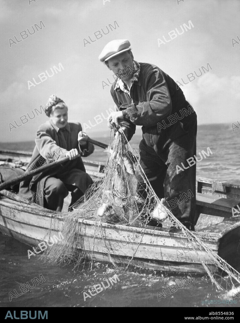 Orig. bildtext... INGA-LILL ROSSVALD OCH HARRY BRANDELIUS DEN 30/4 53. Inga-Lill ror som en hel karl, men så är hon också född i Tönsberg vid norska kusten. Harry Brandelius har varken motor- eller segelbåt. Att ro stärker konditionen, menar han. Anm. H Brandelius, 1910-1994, sångare, gift med I Rossvald. I Rossvald, 1920-1988, sångare, musiker. Fiska strömming Båtar Ekor Nät Kepsar Publ i RiR 20/53 persons: INGA-LILL ROSSVALD;HARRY BRANDELIUS sites: SVERIGE.