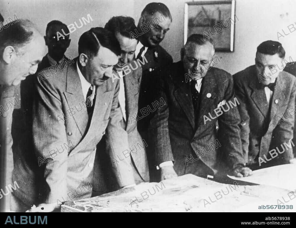 Hitler, Adolf; Politiker (NSDAP). 1889-1945. - Hitler, während eines Besuchs in Bayreuth, besichtigt Modelle und Baupläne für die Umgestaltung der Stadt in der Ludwig-Siebert-Halle. (V. l. n. r., Architekt Reissinger, Hitler, Wieland Wagner, SA-Obergruppenführer Brückner, Gauleiter Wächtler u. Ruckdeschel.- Foto, 4.8.1939.