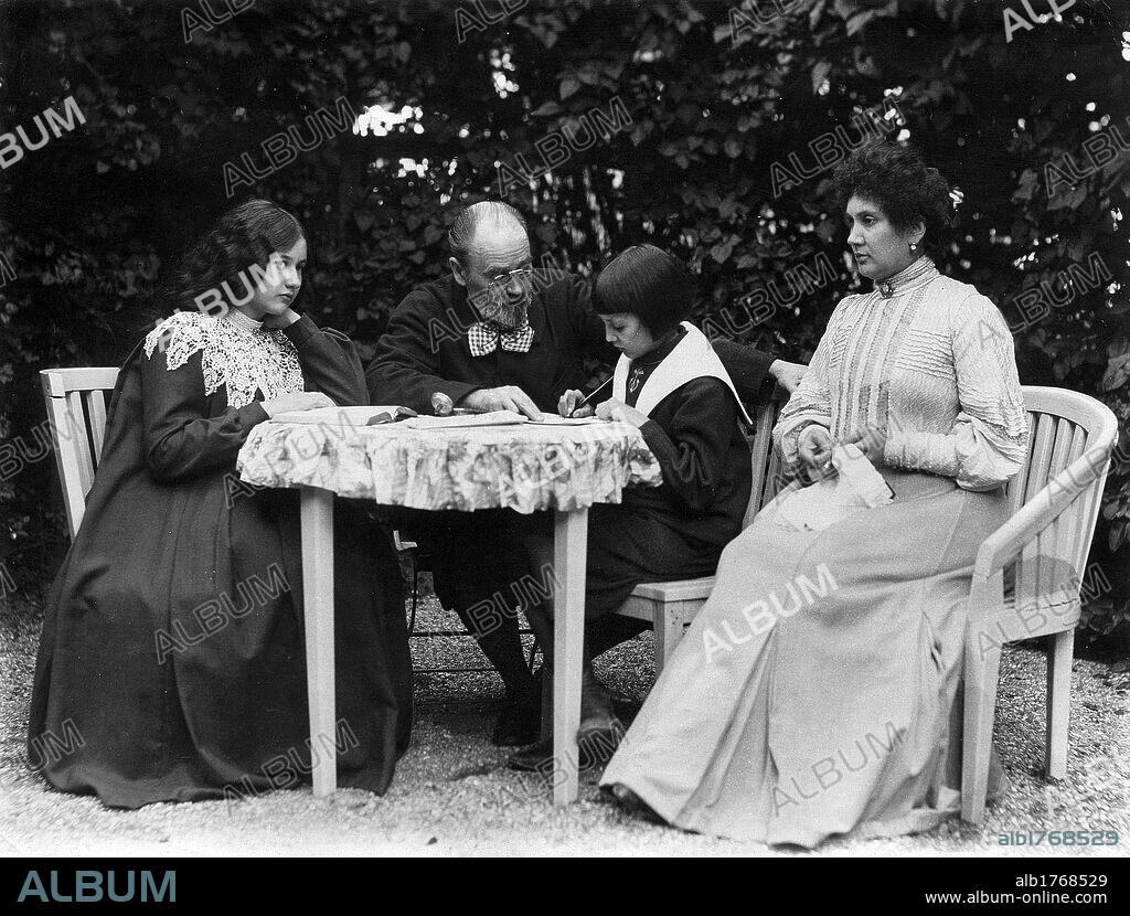 Emile Zola sitting in his garden. French writer Emile Zola sitting at a table in the garden of his house between his children, Jacques e Denise, and with his partner Jeanne Rozerot. Verneuil, 1890s.