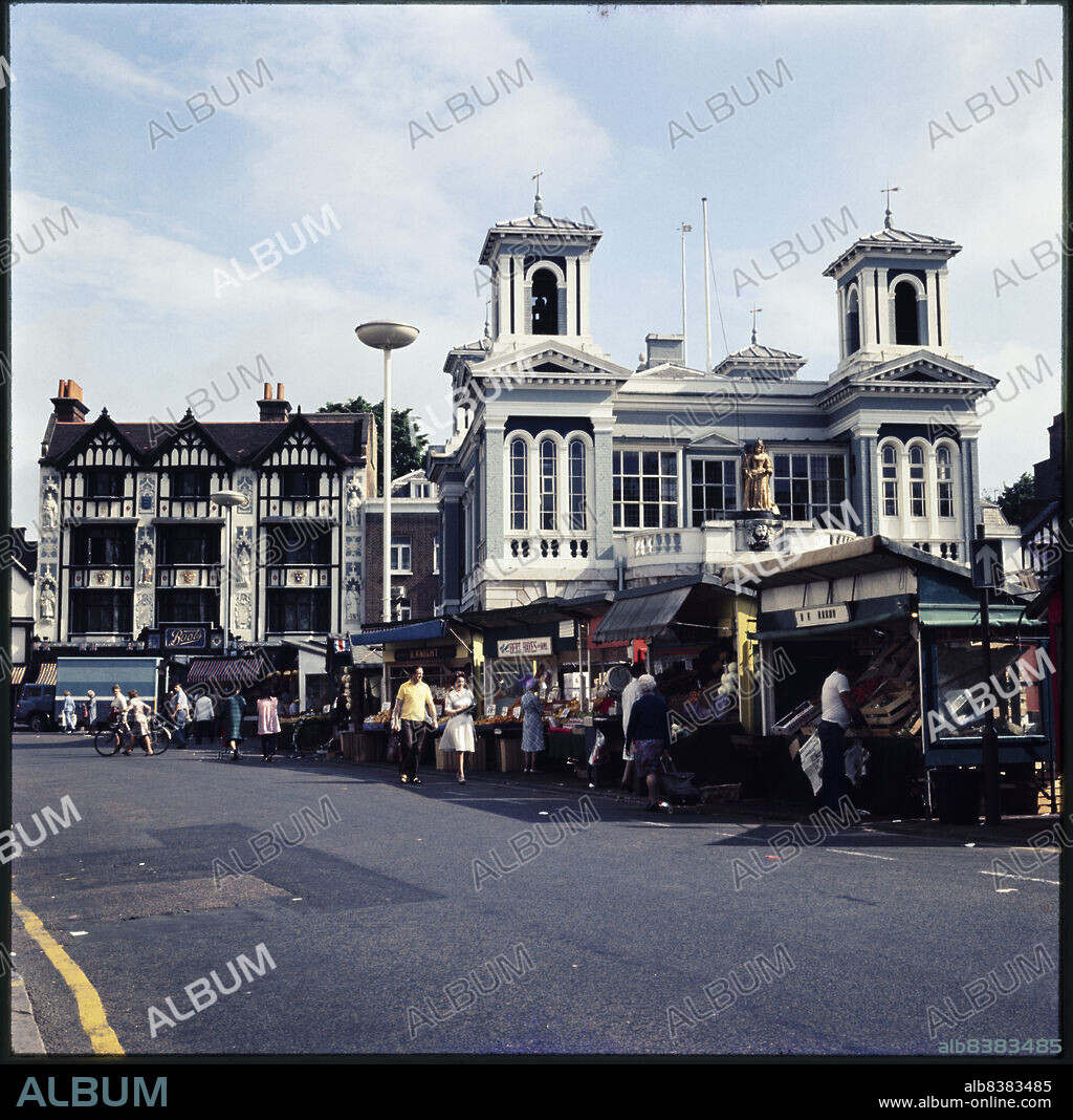 NICHOLAS ANTHONY JOHN PHILPOT. Market Place, Kingston-upon-Thames, Greater London, Authority, 1970s-1990s. The Market Place in Kingston-upon-Thames, with market stalls set up in front of Market House, and Boots the Chemist at 15-16 Market Place beyond. The Boots shop at 15-16 Market Place was built in 1909 in a Jacobean Revival style, designed by Michael Vyne Treleaven. The statues on the facade and stained glass commemorate the crowning of the Saxon kings in Kingston.