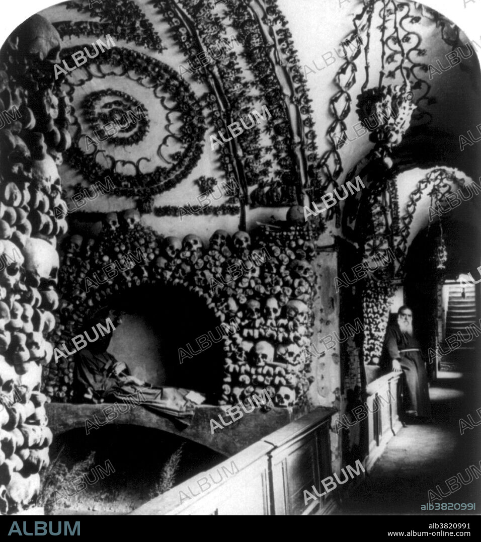 Stereograph shows corridor in the Cappuccini Catacombs, Rome, Italy, 1897. The Capuchin Crypt is a small space comprising several tiny chapels located beneath the church of Santa Maria della Concezione dei Cappuccini on the Via Veneto near Piazza Barberini in Rome, Italy. It contains the skeletal remains of 3,700 bodies believed to be Capuchin friars buried by their order. The Catholic order insists that the display is not meant to be macabre, but a silent reminder of the swift passage of life on Earth and our own mortality. When the monks arrived at the church in 1631, moving from the old monastery, they brought 300 cartloads of deceased friars. Fr. Michael of Bergamo oversaw the arrangement of the bones in the burial crypt. The soil in the crypt was brought from Jerusalem, by order of Pope Urban VIII. As monks died during the lifetime of the crypt, the longest-buried monk was exhumed to make room for the newly-deceased who was buried without a coffin, and the newly-reclaimed bones were added to the decorative motifs.