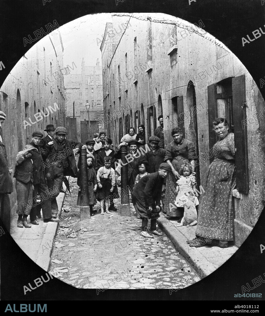 Residents of Little Collingwood Street, Bethnal Green, c1902. Residents of the street pose for the photographer. Two of the boys in the front of the picture are barefoot. A little girl stands on the right, with a dog sitting in the begging position.  Galt came to London in 1890 to work as a missionary for the London City Mission. In the early 1900s he took a series of photographs, mainly of the East End, which he had made into lantern slides to illustrate lectures publicising the work of the Mission. Galt sought to show that though there was great poverty in the East End, the people were not sub-human, as was popularly imagined by the middle-classes, but ordinary folk trying to do their best under difficult circumstances.