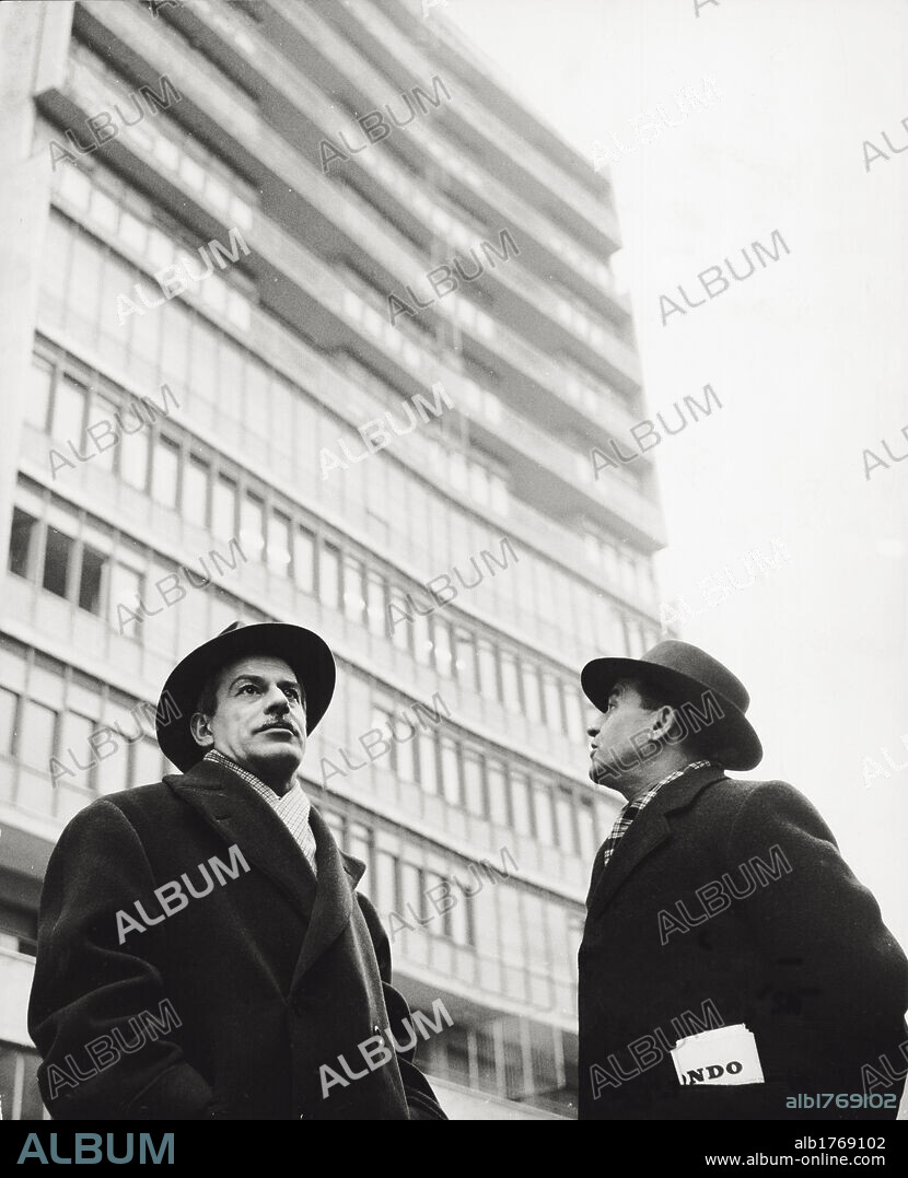 Highbrows Elio Vittorini and Sandro Cruciani. Writers Elio Vittorini and Sandro Cruciani standing in front of skyscraper, looking in opposite direction. Milan, Italy, February 14th, 1955.