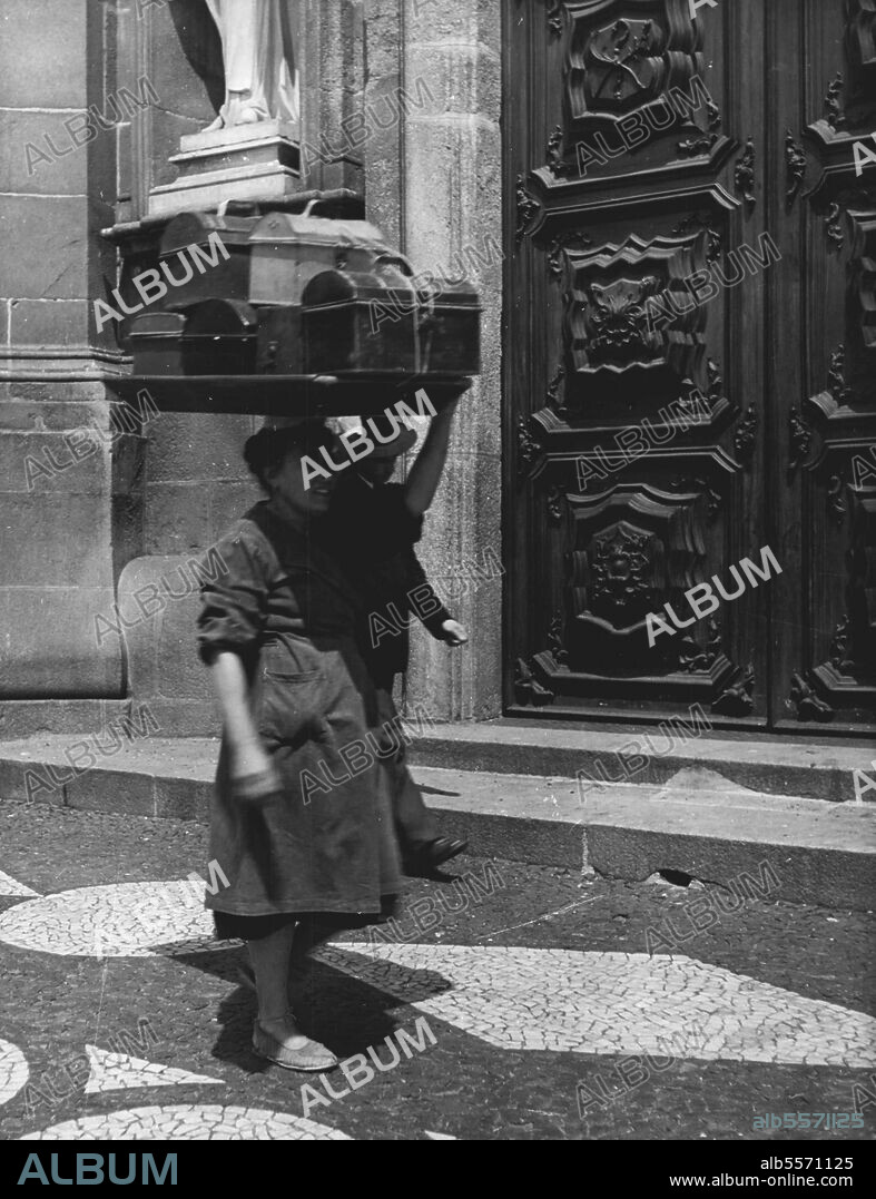 Women Workers Of Portugal -- Much of the porterage is for merchant houses. Here a woman in the business district of Lisbon frowns under the weight of a tray full of dispatch boxes. September 30, 1949. (Photo by Steven Henty, Pictorial Press).
