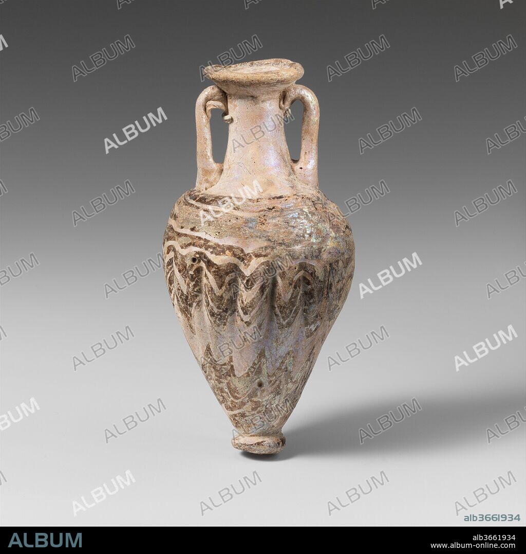 Glass amphoriskos (perfume bottle). Culture: Greek, Eastern Mediterranean. Dimensions: H.: 4 7/8 in. (12.4 cm). Date: late 6th-5th century B.C..
Opaque white, with handles and base-knob in same color; trails in translucent purple.
Deeply inward-sloping rim-disk; cylindrical neck tapering upward; uneven, sloping shoulder; tall conical body; large, slanting circular base-knob with rounded edge and slight indent on bottom; two vertical strap handles drawn up from shoulder, turned in, and pressed on to underside of rim-disk and top of neck.
One thick, rounded trail attached at edge of rim-disk; another trail applied on shoulder and wound round spirally, at first  in horizontal lines, then tooled into an irregular zigzag pattern from the greatest diameter of the body to the base-knob, with deep vertical tooling indents around upper body; another trail applied to edge of knob-base.
Complete, except for weathered chip in base-knob; some pitting of large bubbles, and iridescent creamy weathering covering all surfaces, obscuring trail pattern on body.
Two-handled vase with zigzag pattern.