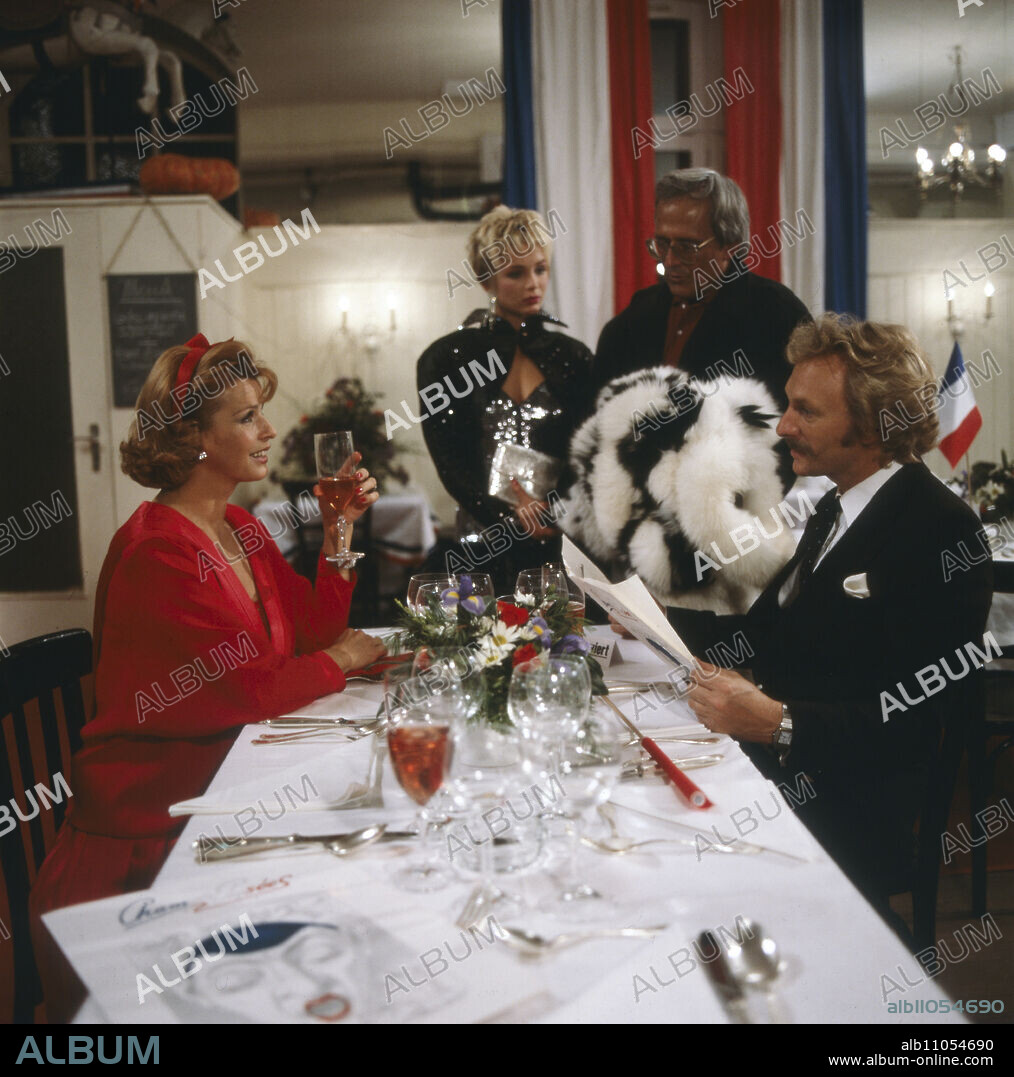 Senta Berger as Mona sitting at the table with Franz Xaver Kroetz as Baby Schimmerlos, in the background Corinna Drews as Lisa and Dieter Hildebrandt as Herbie in Kir Royal, Episode 1: Wer reinkommt, ist drin, Director: Helmut Dietl, 1986.