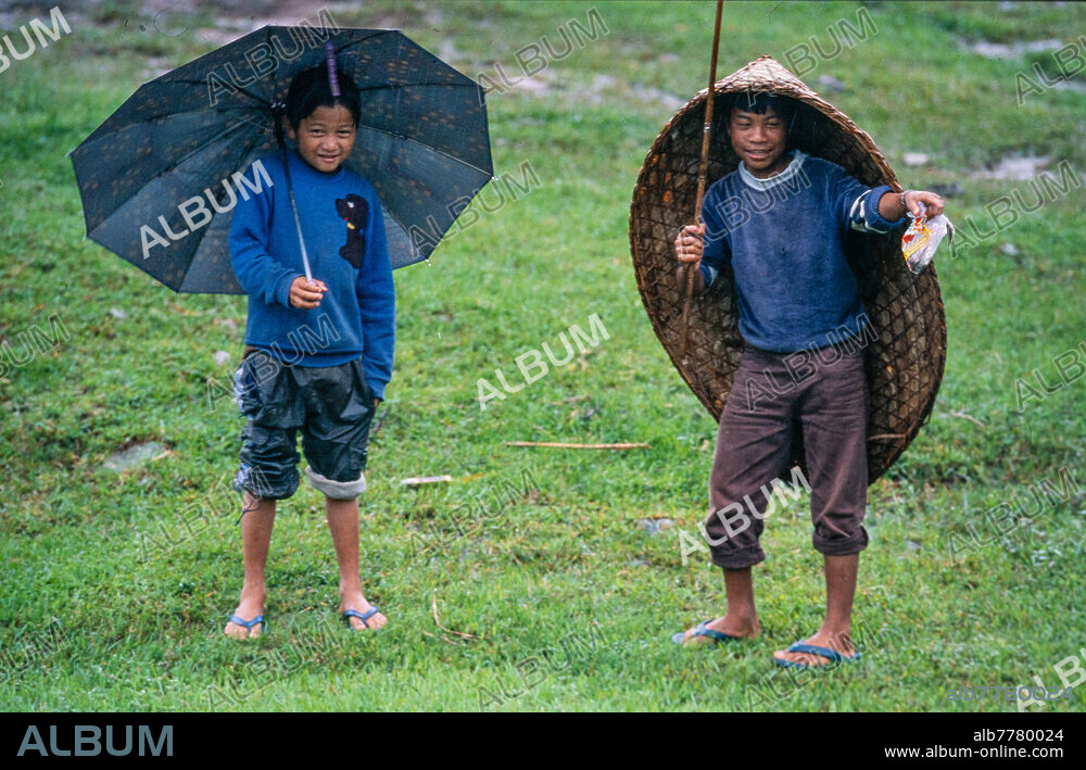 India / children. - In the state of Meghalaya, north-east India, during the monsoon season: two boys with a fishing rod, umbrella and bamboo umbrella (kunup) in the rain. - Photo, 2004.