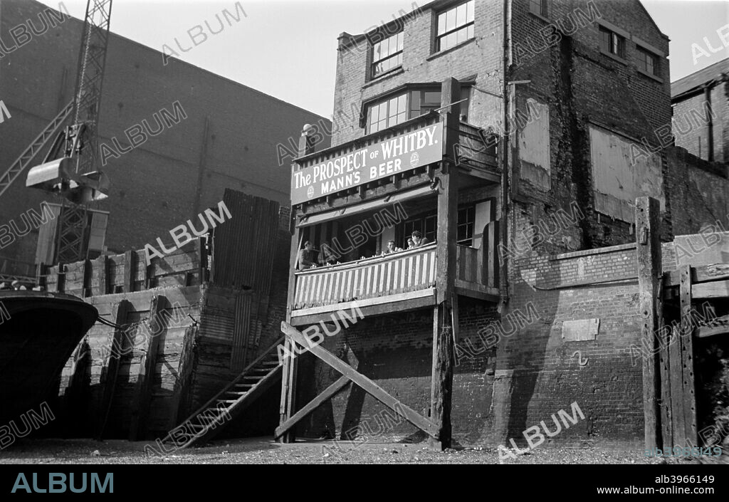 The Prospect of Whitby, 57 Wapping Wall, Shadwell, London, c1945-c1965. Seen here from the River Thames, customers sit on a balcony over the beach at low tide. One of the oldest riverside public houses in London, the Prospect of Whitby first opened in 1520. It was later named after a ship moored outside in the late 18th century. It originally had a reputation as a haunt of thieves and smugglers; Pepys and Dickens were customers, as were painters such as Turner.    .