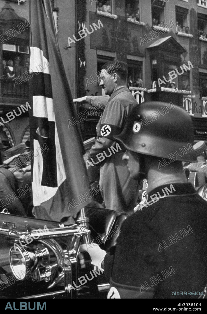 The Blood Flag of 1923, Nuremberg, Germany, 1936. Adolf Hitler (1889-1945) in Nuremberg for the Nazi Party Congress, with a flag commemorating the failed Munich Beer Hall Putsch of 1923. A print from Adolf Hitler. Bilder aus dem Leben des Führers, Hamburg: Cigaretten/Bilderdienst Hamburg/Bahrenfeld, 1936.