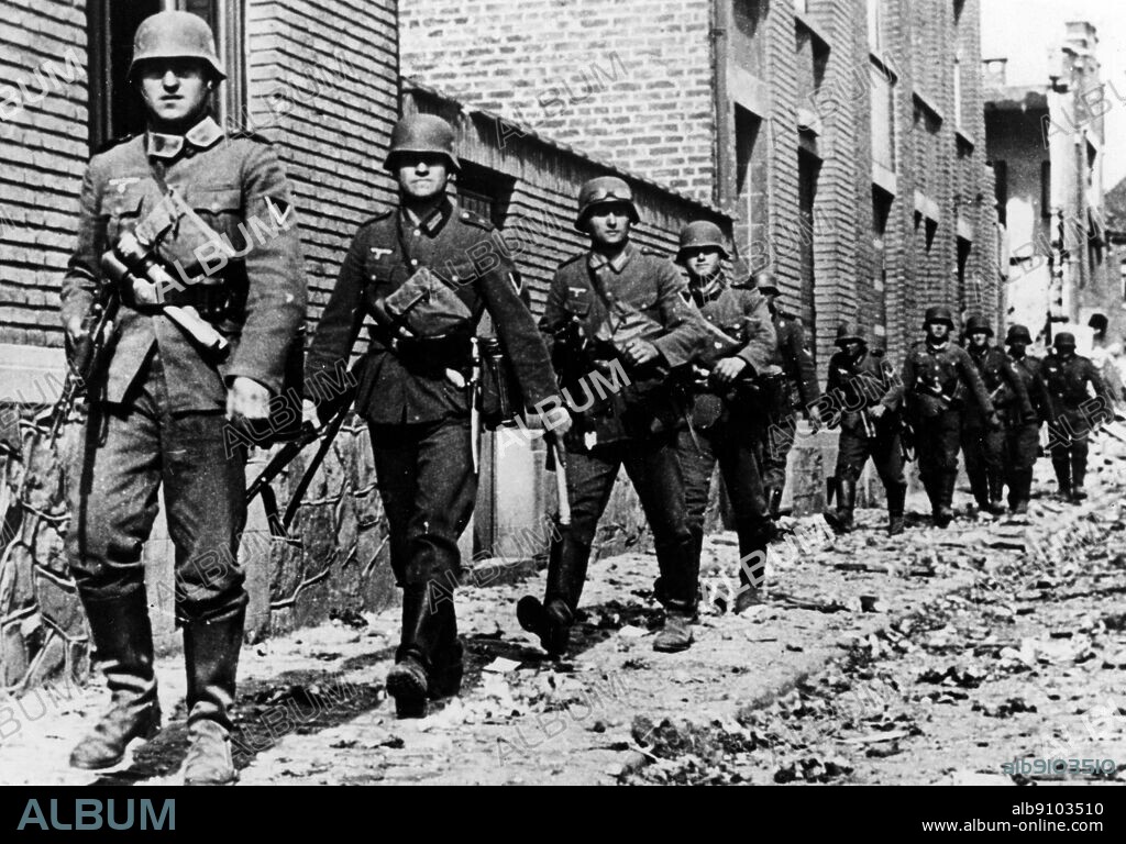 WW2: German troops. Rifle section of motorised infantry unit moving up through a Belgian village street, May 1940.
