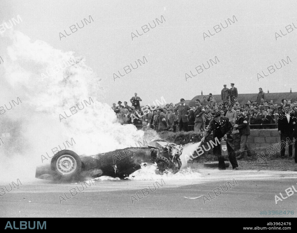 Tony Brooks' car on fire at the British Grand Prix, Silverstone, Northamptonshire, 1956. Brooks' BRM spun and overturned on lap 40 and caught fire. He was thrown clear of the car and fortunately avoided serious injury. A marshall tries to extinguish the fire.