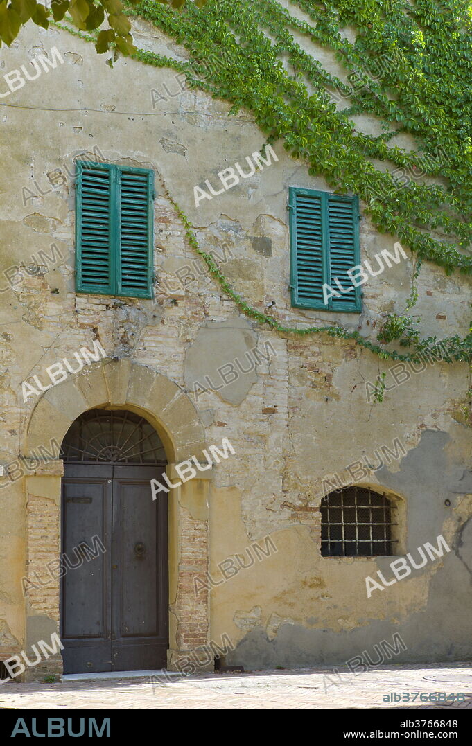 Traditional house with green window shutters and covered in Virginia Creeper, in hill town of Monticcheillo, Val D'Orcia area of Tuscany, Italy.