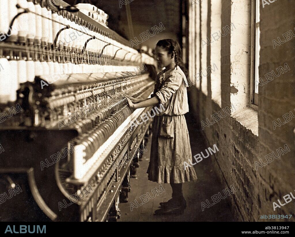 Entitled: "One of the spinners in Whitnel Cotton Manufacturing Company. She was 51 inches high. Had been in mill 1 year. Some at night. Runs 4 sides, 48 cents a day. When asked how old, she hesitated, then said "I don't remember." Then confidentially, "I'm not old enough to work, but I do just the same." Out of 50 employees, ten children about her size. Location: Whitnel, North Carolina." Cotton mills were designed to move cotton through a precise series of production processes that separated, straightened, and twisted cotton fibers, combined them into yarn, then wove the yarn into cloth. Workers directed four or more slivers through a series of rollers in the head of a drawing frame, where they were combined in a single strand. As bobbins on the spinning frames filled with thread, doffers replaced them with empty ones. The spinner's job was to move quickly up and down a row of machines, repairing breaks and snags. Photographed by Lewis Hine, December 1908.