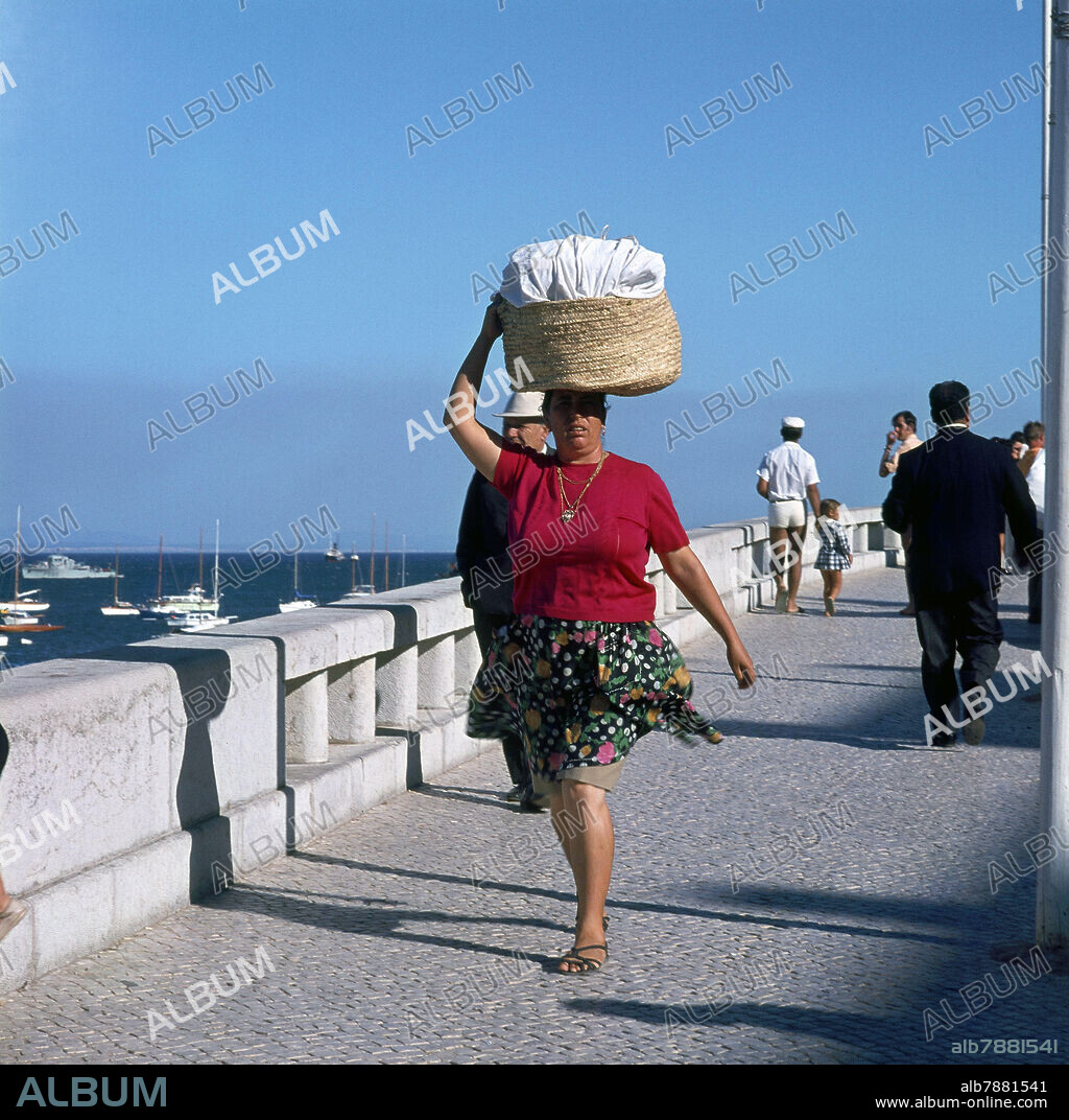 MUJER LLEVANDO UNA CESTA EN LA CABEZA EN EL PASEO DEL PUERTO DE CASCAIS.