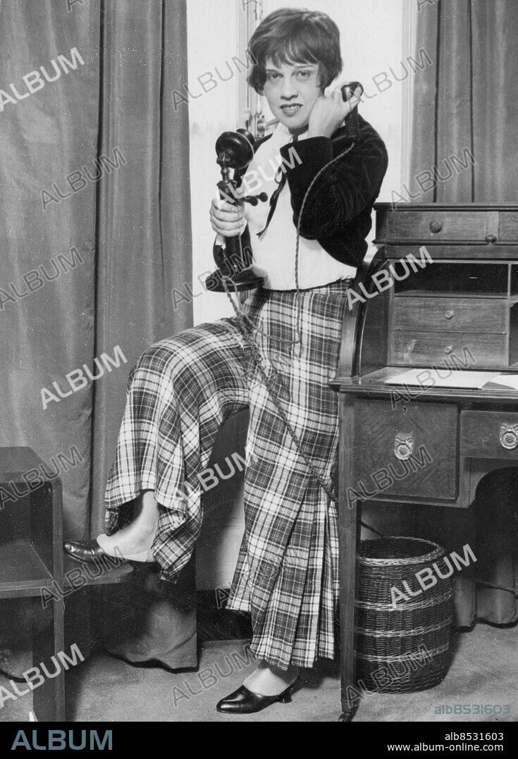 Orig. bildtext... ANITA LOOS SETS NEW FASHION IN SMOKING SUITES FOR WOMEN. Anita Loos, the author of Gentlemen Prefer Blondes, which brought her fame throughout the world, is now visiting London. In private life she is Mrs. John D. Emerson, wife of the American Master of Equity, an organisation controlling the destinies of British theatrical folk. Anita Loos has set a startling new fashion for women - she has a amrt smoking suit - white silk blouse and black velvet smoking jacket, with tartan trousers. The trousers are full and pleated below the knee. Photo shows: Anita Loos wearing her smart smoking suit in the room of her hotel in London. Anm. A Loos, 1893-1981, amerikansk författare Långbyxor Byxor Rutigt Baldwins England CD164 persons: Anita Loos sites: LONDON ;STORBRITANNIEN ;USA*.