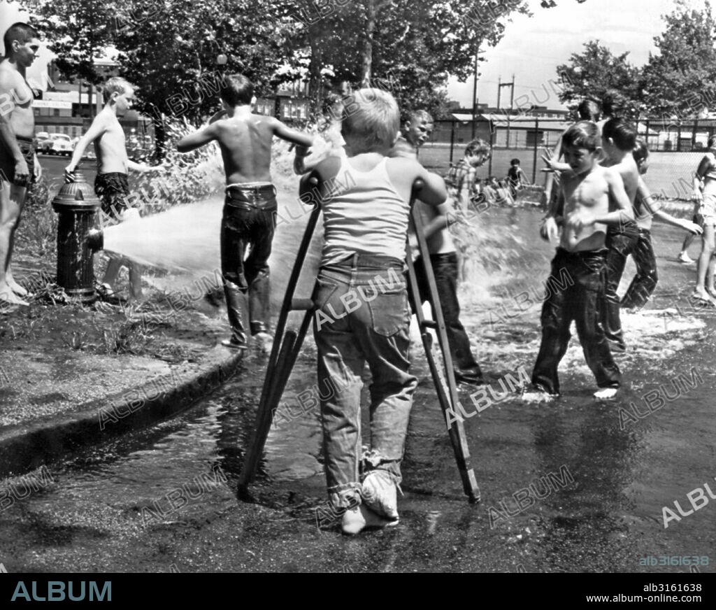 St. Louis, MIssouri: August 1, 1961. A ten year old boy with a broken leg in a cast can only watch as his playmates cool themselves in the heat of the day in the spray from a fire hydrant.