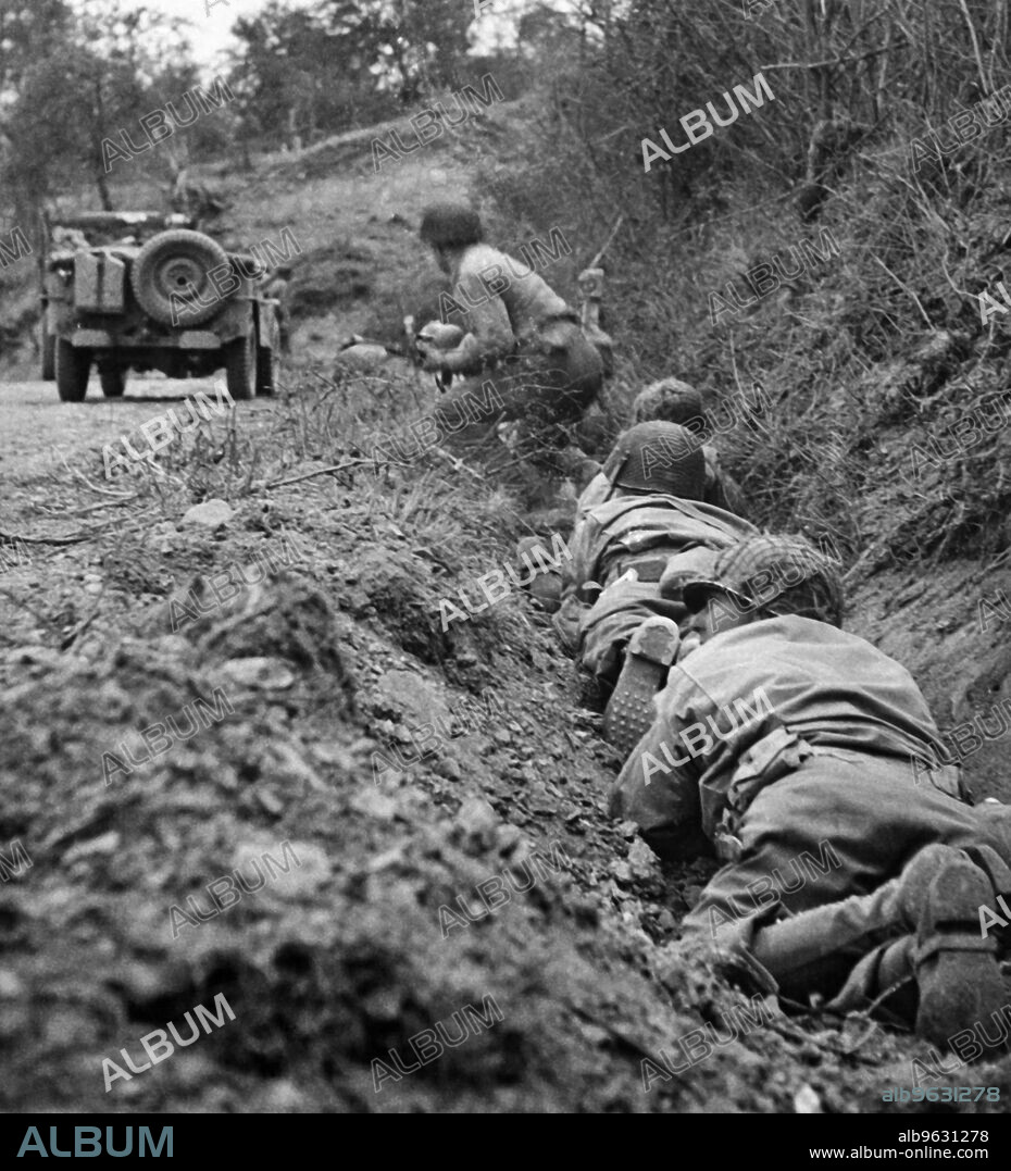 Saint-Lo, France, July 24, 1944 American soldiers inch forward in their fox-hole along the side of a road, while they dodge German mortar and machine gun fire.
