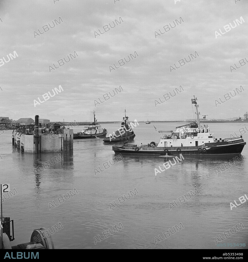 JOHN LAING PLC. A view of the gates of the dry dock at Graythorp being removed by three tugs, prior to the launch of Graythorp I. In the early 1970s Laing Pipelines Offshore constructed the Graythorp fabrication yard and dry dock on the site of the old William Gray Shipyard. The company created a dry dock which was used for the construction of fixed platform North Sea drilling rigs for the BP North Sea Oil Project. Graythorp I had its christening ceremony on June 4th and was launched on Saturday 29th June 1974, heading off for the Forties Oil Field 250 miles away. The tugs shown in the photograph included the Schouwenbank and the Banjaardsbank, both from Rotterdam.
