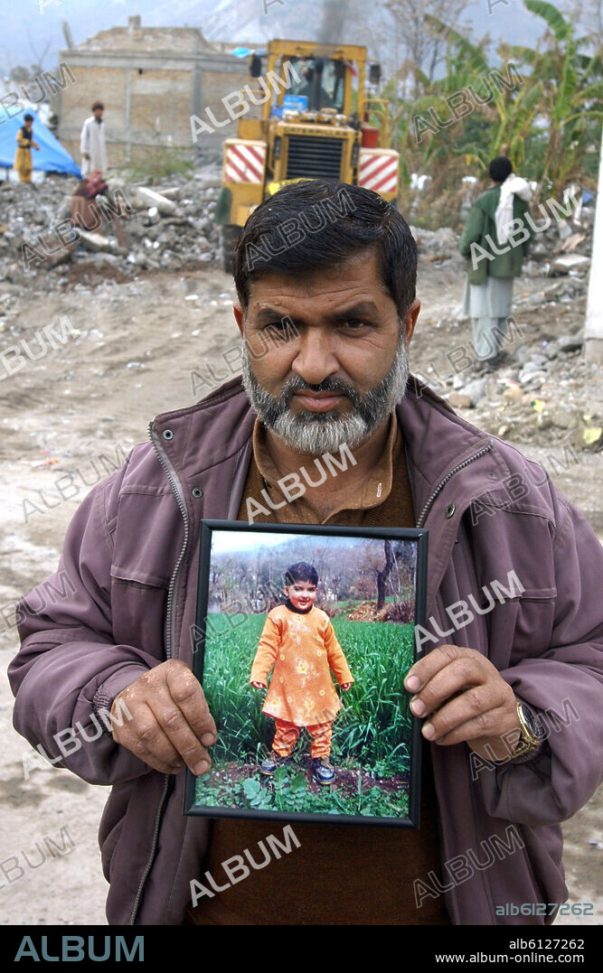 A father shows a picture of his little daughter, who was buried dead by debries after her school had collapsed in Muzaffarabad, Pakistan, Monday, 30 January 2006. In the background a shovel dozer is removes debries. The north-eastern province of Cashmere, Pakistan had been hit by an earthquake of the strength of 7,6 on 8 October 2005. Nearly 80.000 people had been killed, more than three millions were made homeless and suffered severely due to the cold winter. Photo: Wolfgang Langenstrassen. 30/01/2006