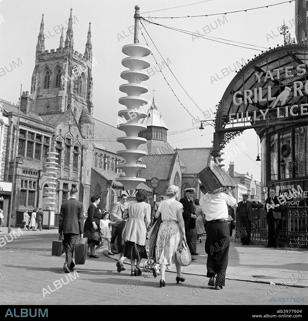 Holidaymakers make their way from the Promenade towards Talbot Road Station on the London & North Western Railway, Blackpool, c1946-c1955. The Church of the Sacred Heart contrasts with the futuristic decorations that adorn the post carrying the illuminations.