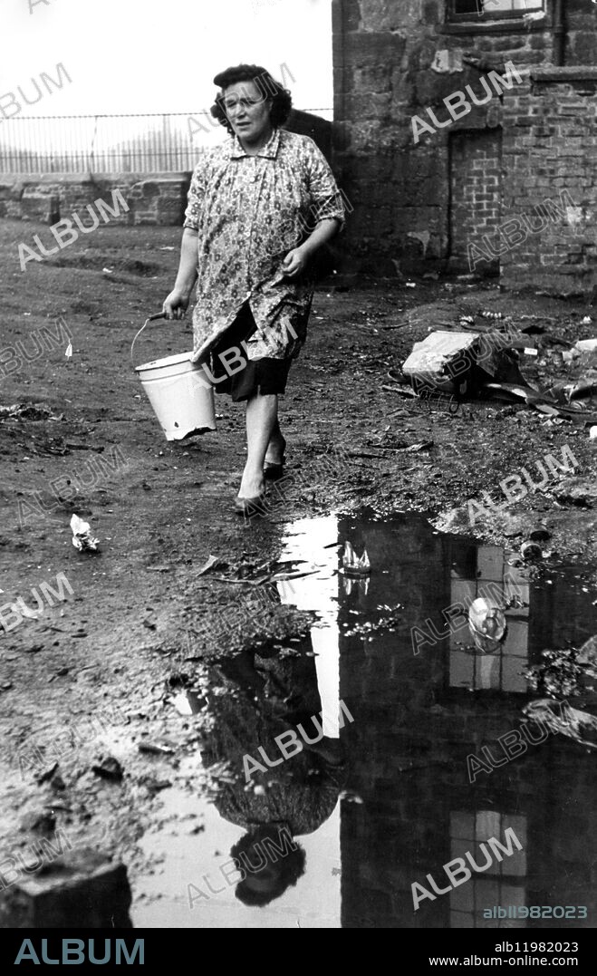 The Gorbals , Glasgow , Scotland. 46 year old James Docherty lives with his wife Margaret , adn their seven children in a "single end " measuring 18 ft x 15 ft on the first floor of 14 Lawmoor Street , a recently condemned property . Mrs Docherty keeps the family spotlessly clean . She is expecting another child shortly . The corridor to the back of the house is flooded so every day she , or one of her chidlren , walks round the tenement buidling to carry the waste to a dustbin . 1952.