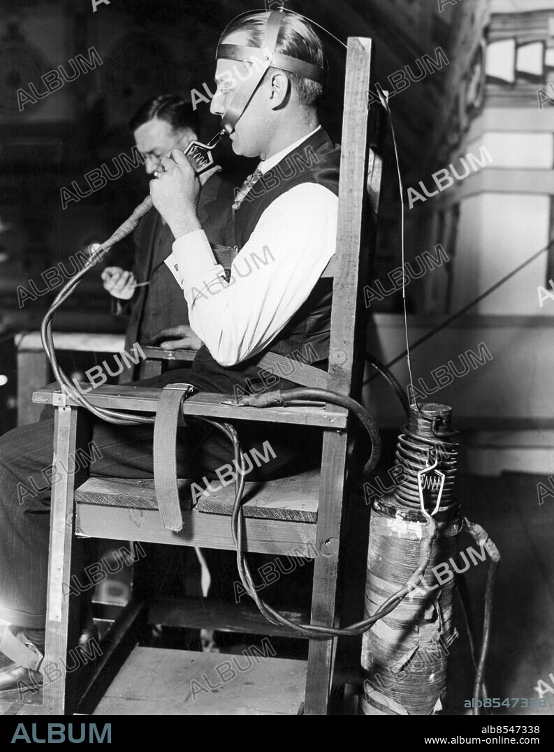 Orig. bildtext... CLAIMS IMMUNITY FROM ELECTRICITY. To prove that he is immune to a high voltage of electrical current, Bernays Johnson, noted electrical engineer allows 2200 volts or 350 amps of electricity to pass thru his body while seated in an electric chair fitted with necessary attachments. In this demonstration at the Chicago Radio Show, he also shows that the current used is three times greater that that used to electrocute a senteced prisoner, by holding an iron bar between his teeth, which become red hot when the current is turned on. Photo shows Johnson being timed to see how long he can remain with the juice on. Anm. CD93 Experiment Mätningar persons: Bernays Johnson sites: CHICAGO ;USA.