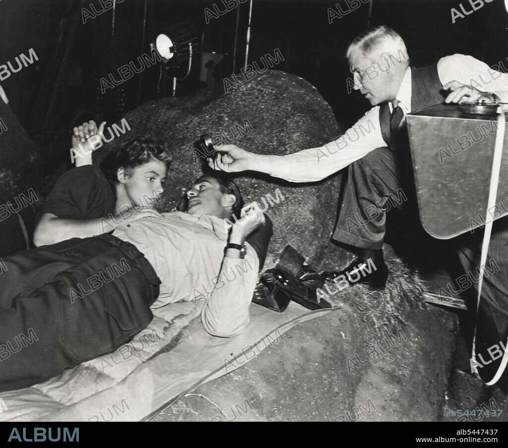 Technicolor Cameraman Ray Rennahan steps into the picture with his light meter to test light conditions because the daylight ***** is now turned into night. March 01, 1944.