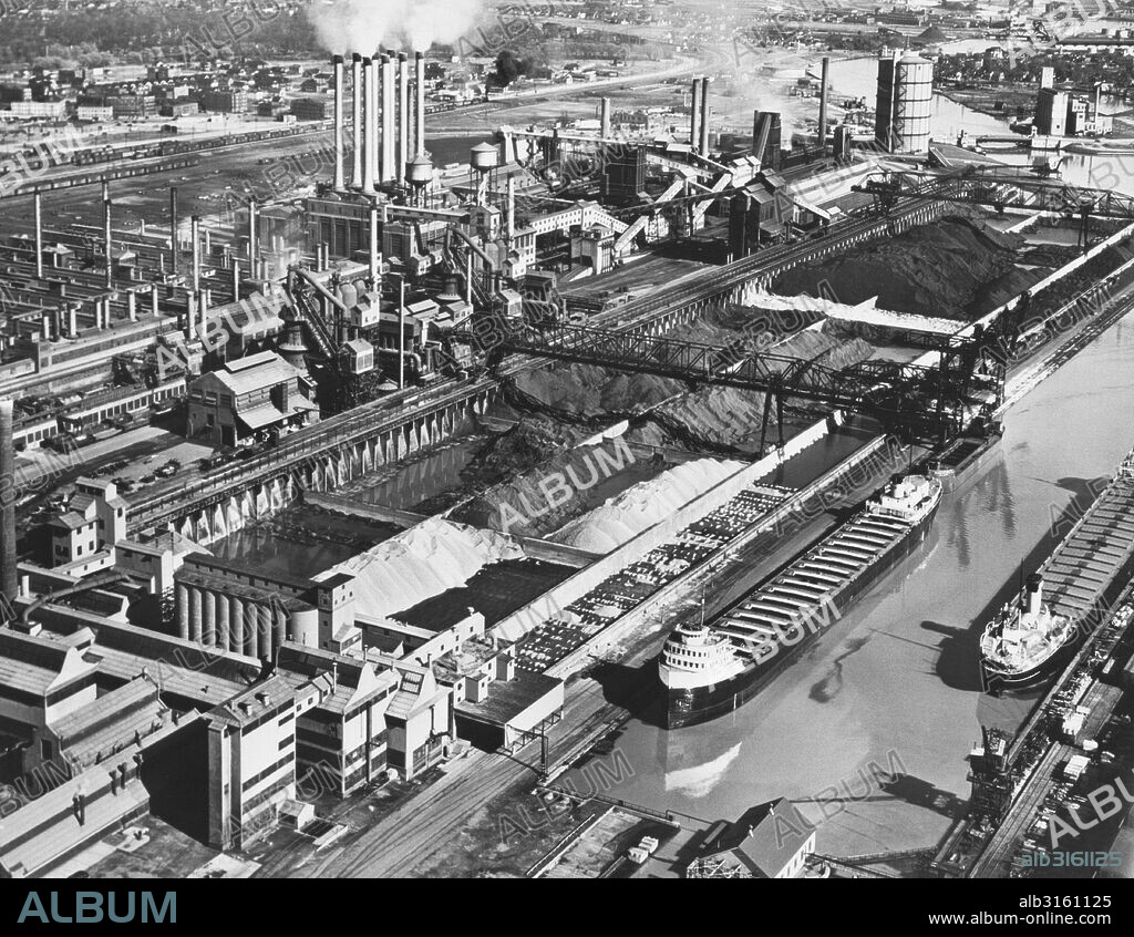 Dearborn, Michigan: May, 1947 Ford Motor Company's River Rouge plant showing the stockpiles of iron ore, coal and limestone which supply the the blast furnaces, foundry and powerhouse in the background. Two iron ore carriers are at the dock to the right.