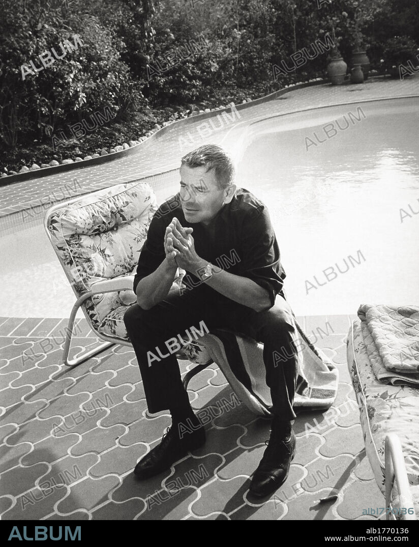 Glenn Ford photograped in his villa. Actor Glenn Ford sitting in the garden in his villa in Beverly Hills. Behind him, there is a swimming pool. Beverly Hills, USA, 1965.