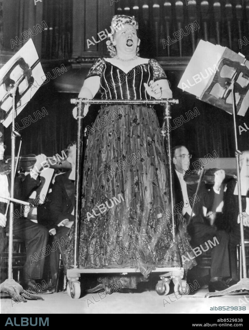 Orig. bildtext... FAMED DIVA BACK ON HER FEET IN ELECTRA. CHICAGO, ILL....STRICKEN WITH INFANTILE PARALYSIS IN 1941, MARJORIE LAWRENCE, FAMED AUSTRALIAN SOPRANO, SANG ON HER FEET LAST NIGHT FOR THE FIRST TIME IN SIX YEARS. SHE IS SHOWN SINGING THE TITLE ROLL IN RICHARD STRAUSS' ELECTRA AT CHICAGO ORCHESTRA HALL, WHERE SHE DREW TUMULTUOUS APPLAUSE FOR HER PERFORMANCE. MISS LAWRENCE SANG FROM A RAILED CART WHICH GAVE HER SUPPORT WHILE ON-STAGE. THE CART WAS WEELED BY HER HUSBAND, DR. DONALD KING. Orig. bildtext... INFANTILE PARALYSIS VICTIMS STANDS FOR ROLE. Chicago, Ill. Marjorie Lawrence, noted Australian soprano, stood thursday night for the first time in six years to sing the title role in Richard Strauss Elektra. The 38-year-old blonde star who was stricken in 1941 with infantile paralysis, drew a tumultuous applause from Chicago's packed orchestra hall for her performance. Her previous concerts had been given from a wheel chair after she recovered enough from the polio attack to go back to the concert stage. She is shown during the one-act opera, supported by a railed chair which was pushed on to the stage by her husband, Dr. Donald King. Anm. Lawrence, Marjorie, 1909-1979, australiensisk sångare, sopran, tolkade bl a Wagner, 1941 drabbad av polio Scenkläder Handikapphjälpmedel Stöd Notställ Plattformar Rehabilitering Korpulens Fetma Vokalist Gapa Föreställningar CD396 persons: MARJORIE LAWRENCE sites: CHICAGO;USA;AUSTRALIEN*.