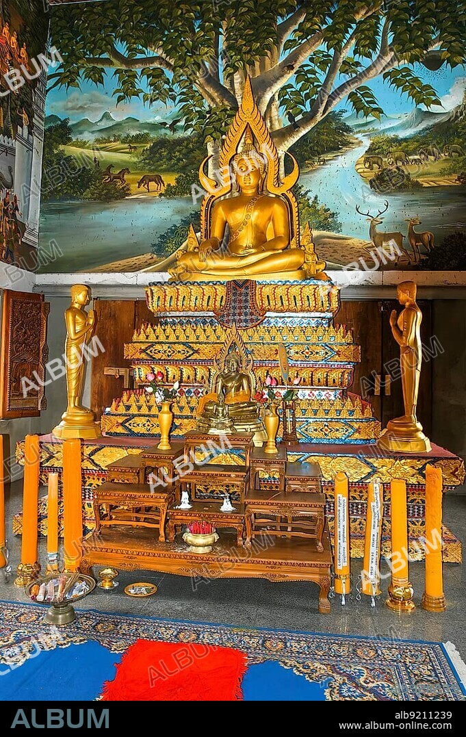 Gilded gold-coloured Buddhist altar with statue of seated Buddha in background mural with deer, Buddhist temple Wat Sri Sunthon, Thalang, Phuket Island, Thailand, Asia.