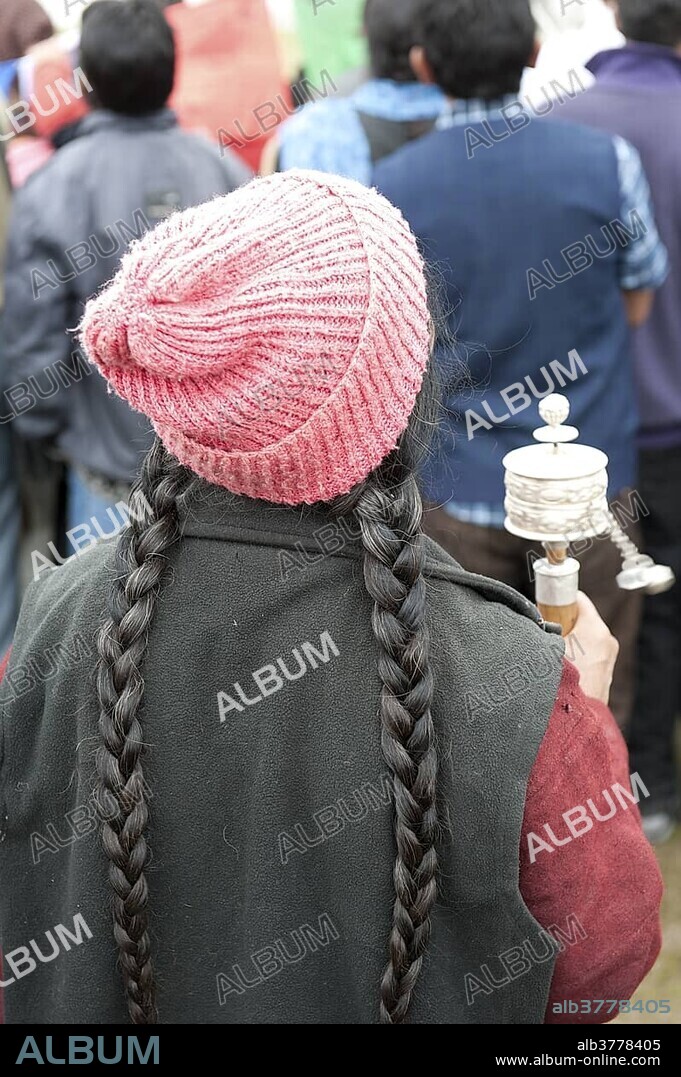 Tibetan festival, elderly woman with braids wearing a hat and turning a prayer wheel, Leh, Ladakh district, Jammu and Kashmir, India, South Asia, Asia.