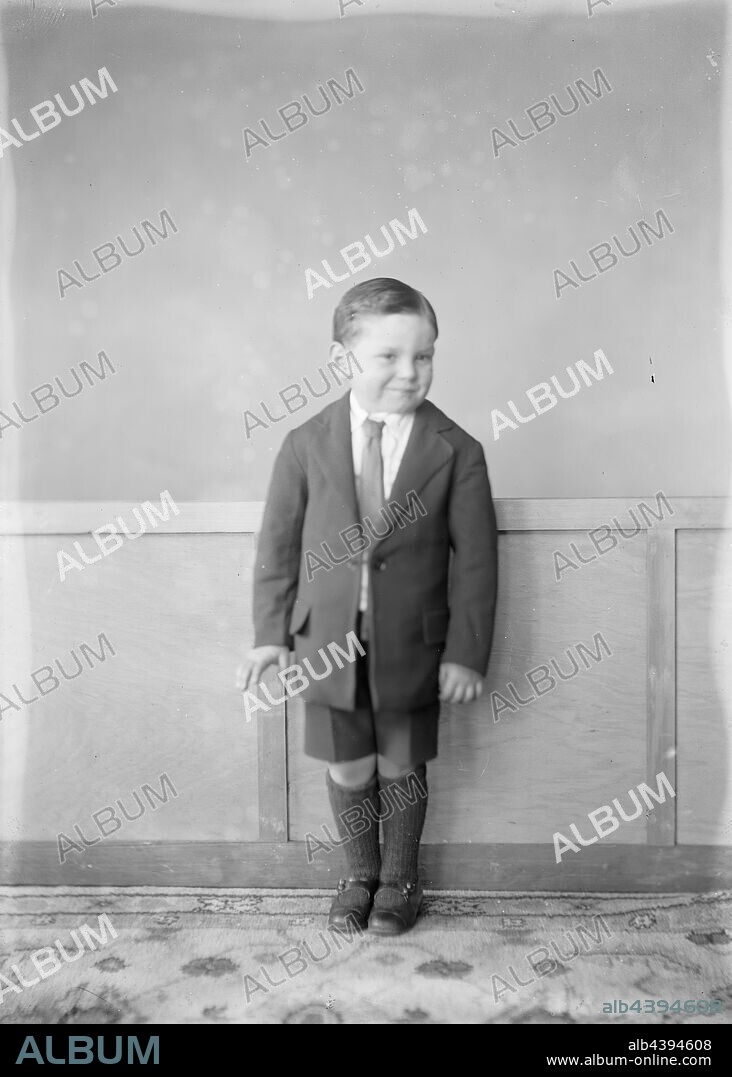 Glass Negative - Boy in Suit, circa 1930s, Black and white, half plate negative featuring a small boy in a suit jacket, formal shorts and long socks, standing in a carpeted hallway against the wainscotting, circa 1930s. He is likely the child of members of the Independent Order of Rechabites, as there are other photos in this group featuring Rechabite members. The provenance of this image is unclear, but it came from the Kodak corporate.