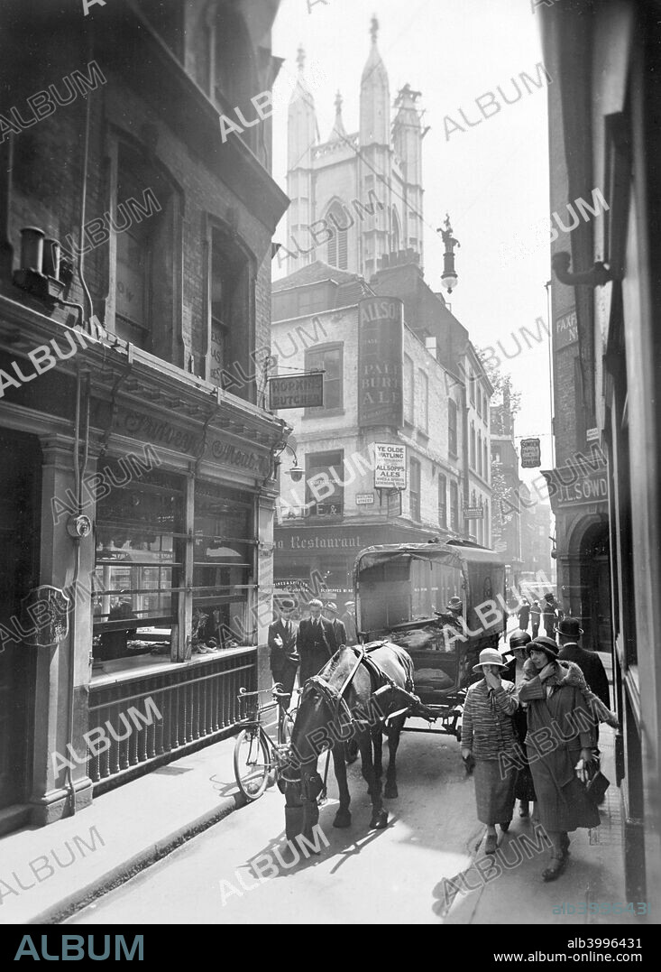 Bow Lane looking south, City of London, c1930. A horse is eating from its nosebag in the narrow lane. The 'Olde Watling' tavern, visible on the corner of of the junction of Bow Lane and Watling Street, was one of the first buildings to be erected after the Great Fire of London in 1666. Behind it rises the tower of St Mary Aldermary, designed by Sir Christopher Wren. Reid, an amateur photographer of independent means, began an ambitious project to record, in photographs and prose, an extended walk through the historic Cities of Westminster and London. By the time of his death in 1933 he had taken over 700 photographs, organised geographically into a series of albums, and had compiled two manuscript books, entitled The Route Ornate, which served to annotate the photographic journey. The photographs are remarkable for their pictorial and technical quality.