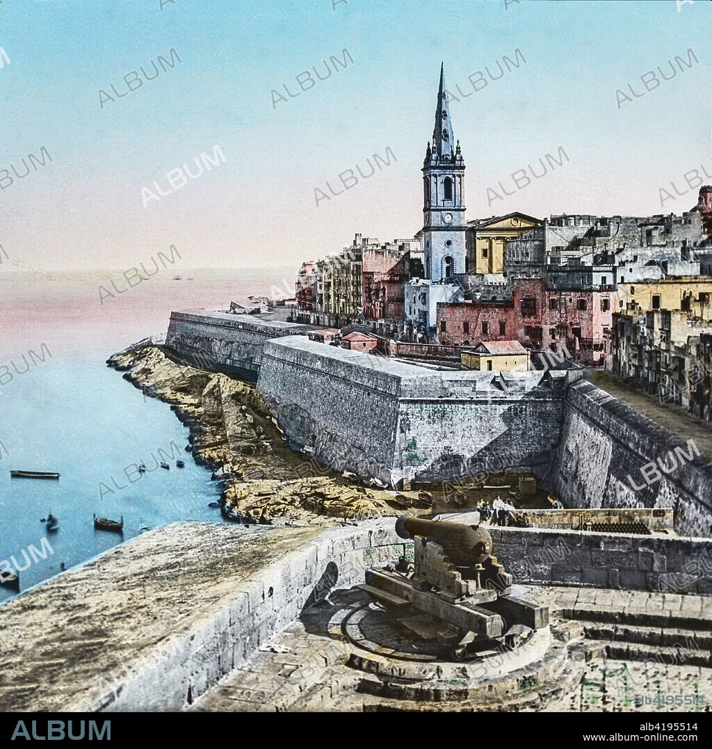 Magic Lantern slide circa 1900 hand coloured. Titled Cities and places of interest in the Mediterranean.39â€”MALTA, MARSA MUSCAT. This is a portion of Yaletta, principally inhabited by the natives, if people can be called natives who have in their veins the blood of half the Southern races of Europe. The houses here are built of the rocky soil of the islandâ€”which is itself but one large rockâ€”and the cultivation of some parts of it (which has been brought to great perfection by continous efforts) is remarkable, when it is remembered what difficulties have to be contended with. On this barren soil all kinds of fruitâ€”including the well-known Maltese orangeâ€”are now grown  as well as corn and hay.