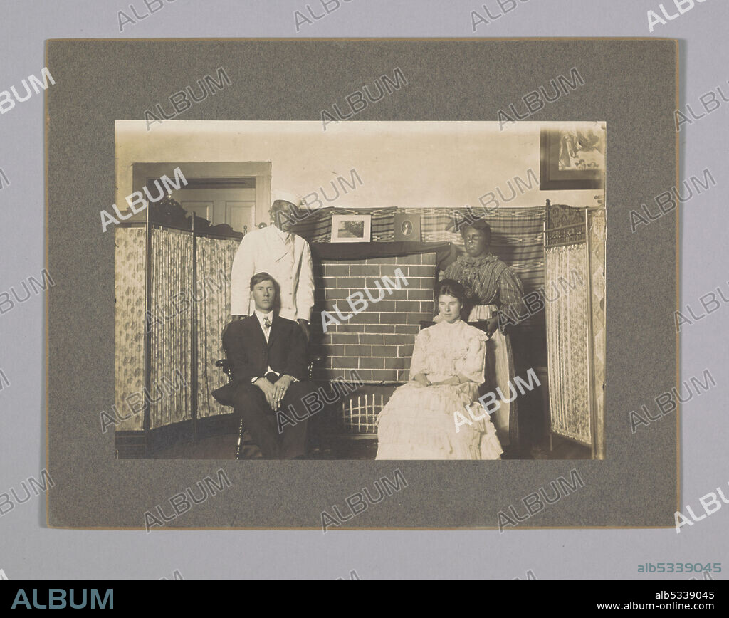 On the proper right side a boy is sitting in a chair. He is wearing a suit and tie. His legs are crossed at the ankles and his hands are on his lap. There is a boy standing behind him. He is wearing a white chef's coat and hat, and is wearing blackface. On the proper left there is a girl sitting in a chair. She is wearing a fancy white ruffled dress. Her dark hair is pulled back and is parted in the middle. Her hands are folded on her lap and she has a bracelet on her proper left arm. There is a girl standing behind her with a striped dress, an apron, and a headscarf. She is also wearing blackface. The boy sitting in the chair is Oliver Howard Horner.