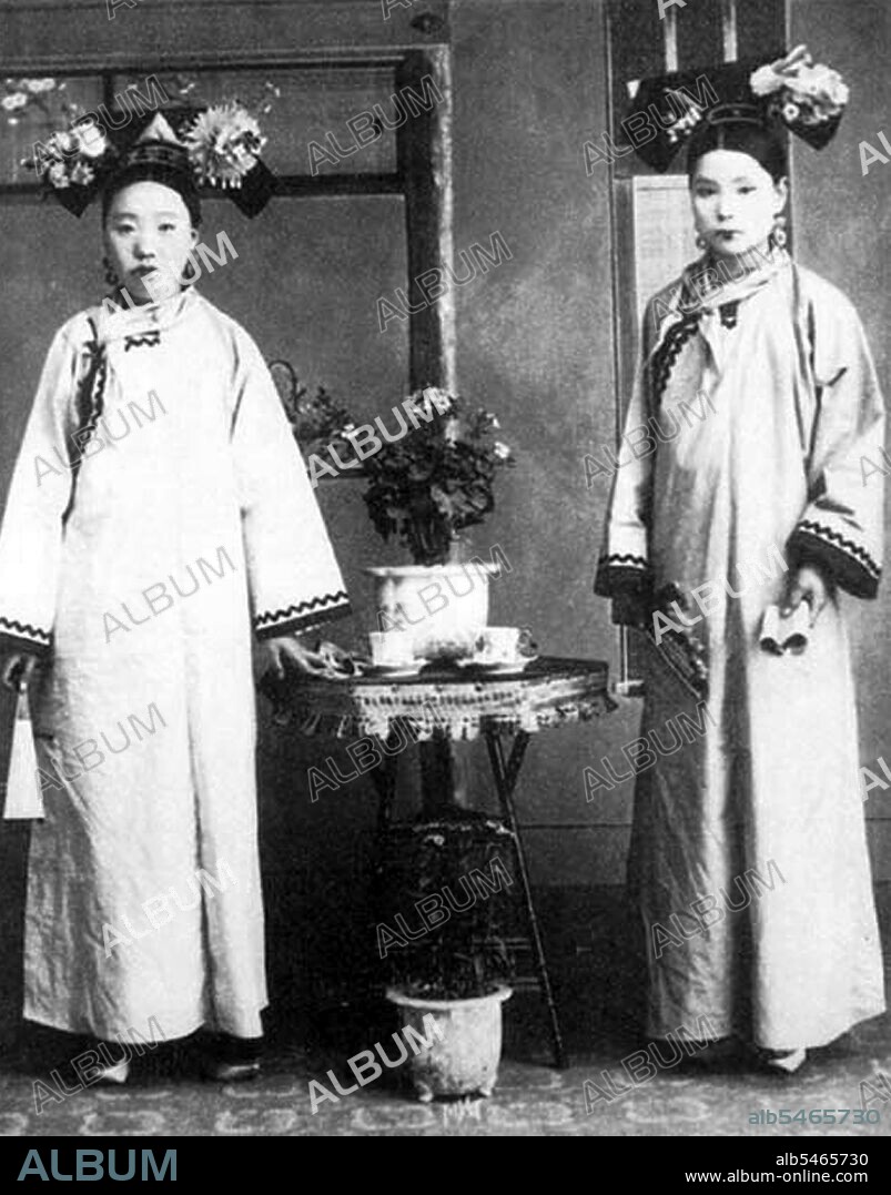 Manchu women of the Forbidden City or Gugong in Beijing pose for a photograph c. 1890 during the Manchu Qing Dynasty (1644-1911). They wear elaborate and expensive dresses. Their faces are whitened with powder, and their lipstick is applied in a narrow band across the centre of their lips following the fashion of the time.