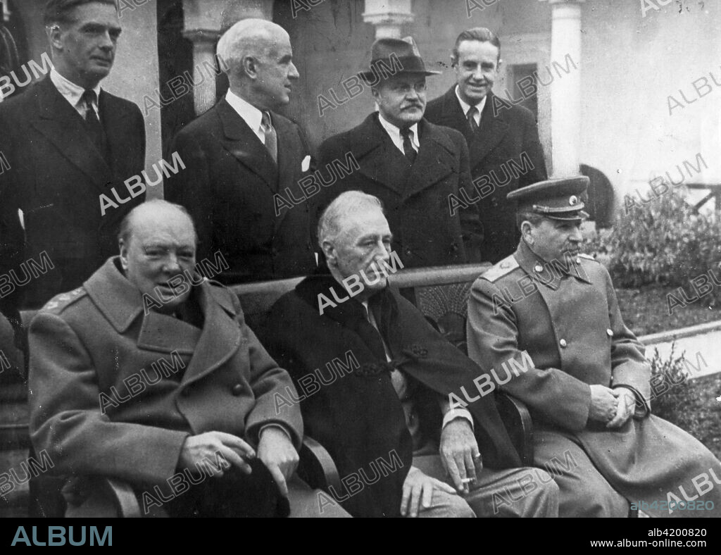 Yalta Conference. Crimea, USSR. February 11, 1945. Prime Minister Winston Churchill of Great Britain, President Franklin D. Roosevelt of the United States and Premier Joseph Stalin of the USSR pictured before the Crimea conference session at Livadia Palace. Behind them, standing, are Eden, Stettinius, Molotov, and Harriman.